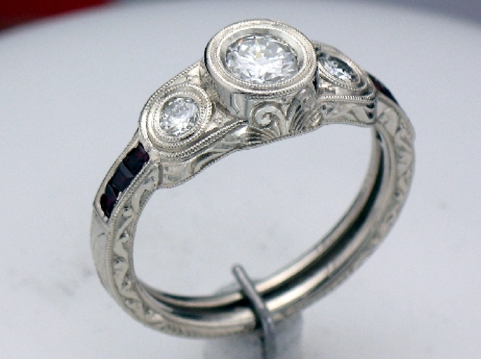 Hand engraved white gold ring with 3 round brilliant diamonds and side baquette rubies.